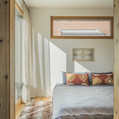 Sonnendurchflutete Zimmerecke mit weißen Vorhängen, einem kleinen Gemälde und Kissen auf einer Bank, die sanfte Schatten werfen.