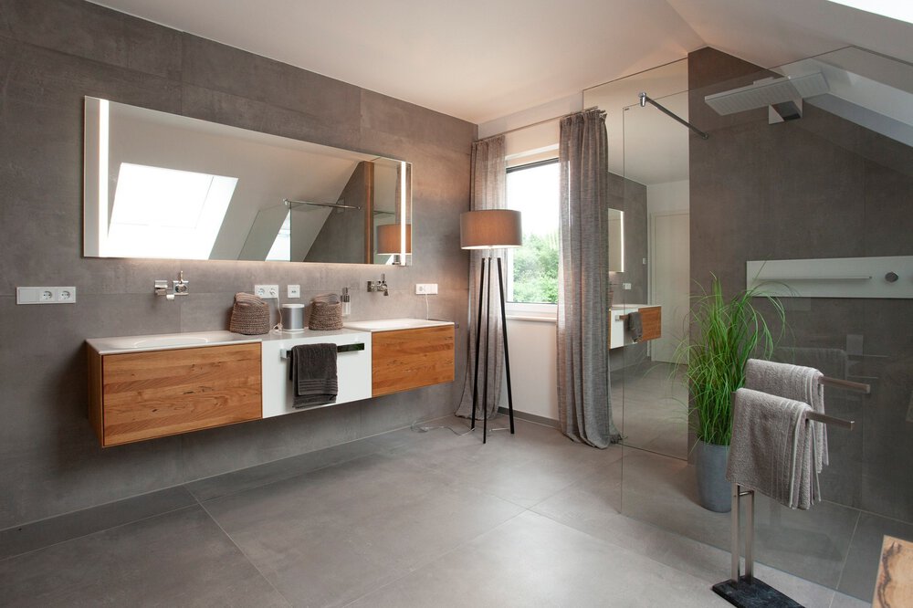 Modernes Badezimmer mit dunklen Fliesen, Holzschränken, großem Spiegel und Oberlichtfenster.
