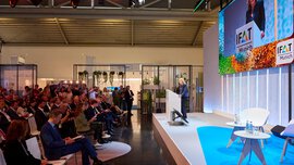 Publikum bei einer Präsentation auf der IFAT Munich, Blue Stage, mit Rednerin am Podium und großer LED-Leinwand im Hintergrund.