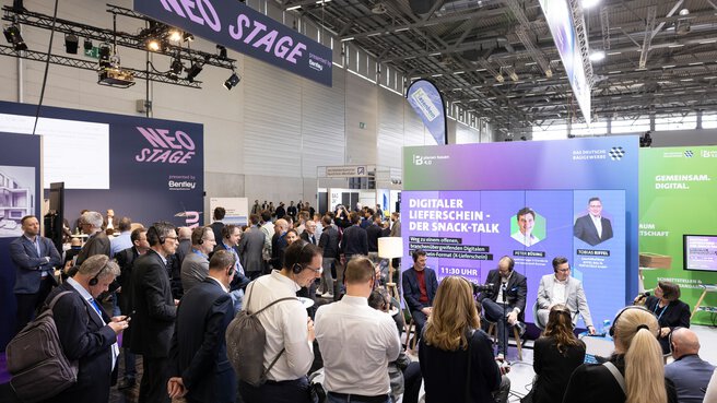 Visitors stand in front of a screen and listen to a panel discussion through headphones. Background screen with the title: Digital Delivery Note – The Snack Talk