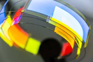 Ein Gebilde aus Kunststoff mit einer reflektierenden, gekrümmten Oberfläche. Die Farben umfassen Rot, Gelb, Blau und Weiß