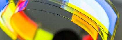 Ein Gebilde aus Kunststoff mit einer reflektierenden, gekrümmten Oberfläche. Die Farben umfassen Rot, Gelb, Blau und Weiß