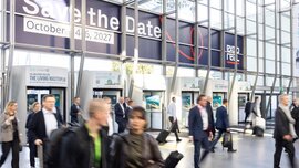 Die Besucher schlendern durch die Eingangshalle eines Kongresszentrums unter einem großen Banner mit der Aufschrift Save the Date: 4.–6. Oktober 2027 und Expo Real.