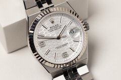 Close-up view of a wide silver angular wristwatch with a serrated edge and a dial with a scaly background.