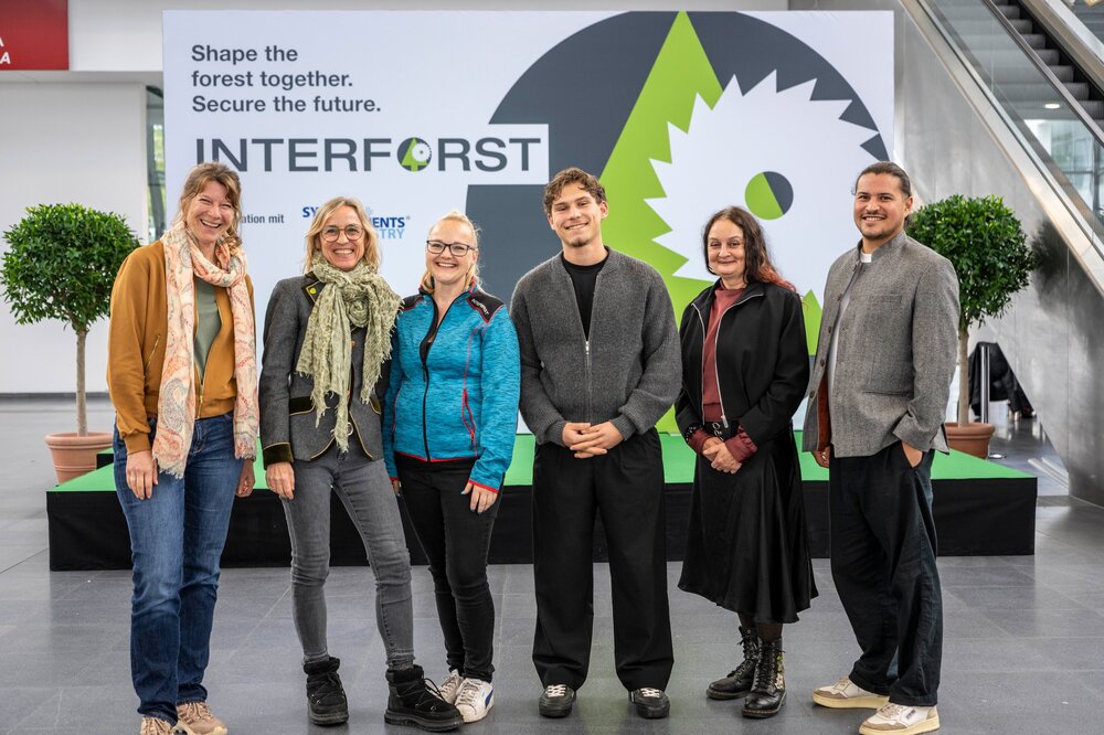 Six people pose for a group photo in front of a large INTERFORST logo backdrop.
