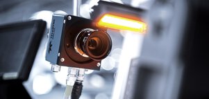 Nahaufnahme einer Überwachungskamera mit einem leuchtenden orangefarbenen Licht über der Linse vor einem unscharfen Hintergrund.