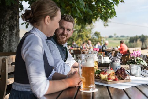 Zwei Personen genießen eine traditionelle Brotzeit in einem Biergarten und erleben die oberbayerische Biergartenkultur.