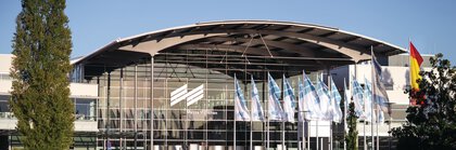 Exterior shot of the west entrance to Messe München with the trade fair lake and flags in the foreground