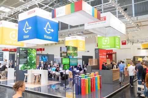 Gut besuchter, farbenfroher Messestand mit Bannern zu den Zielen für nachhaltige Entwicklung.