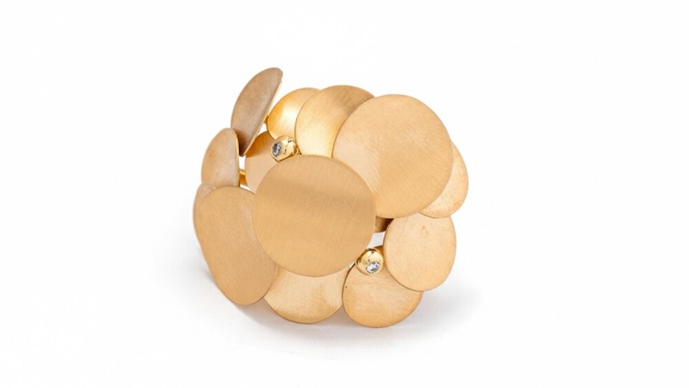 A close-up view of a delicate gold piece of jewelry consisting of gold plates attached to each other with two gemstones.