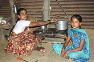 A woman and a child in India sit in front of a simple gas stove