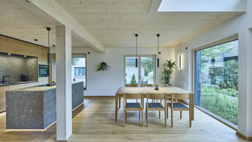 Heller Essbereich mit Holztisch, Stühlen und Hängelampen. Glastüren bieten Blick auf den Garten.