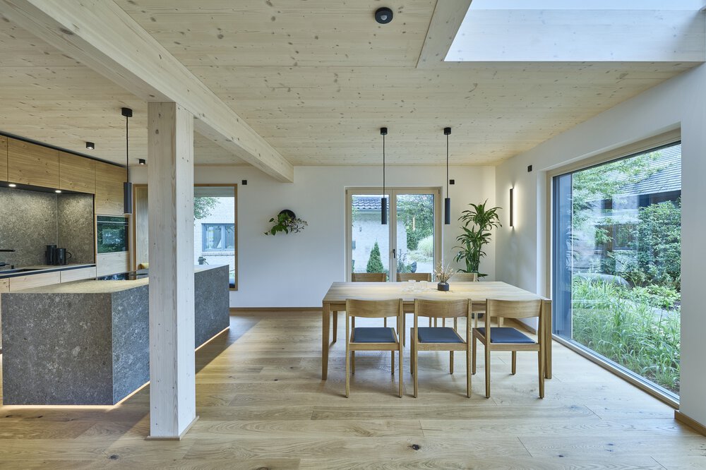 Heller Essbereich mit Holztisch, Stühlen und Hängelampen. Glastüren bieten Blick auf den Garten.