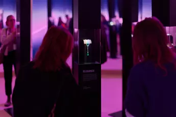 People look at a necklace in a dimly lit exhibition with a pink and purple ambience.