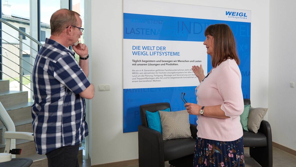 Zwei Personen besprechen in einer modernen Büroumgebung ein Schild zu Weigl Lift Systems.