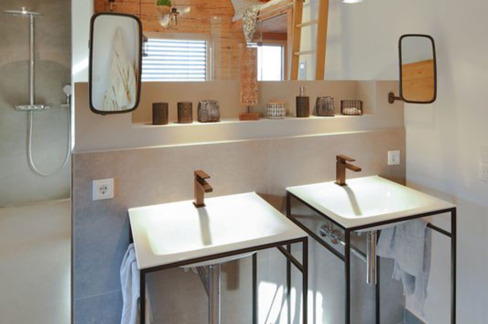 Modernes Badezimmer mit zwei weißen Waschbecken, wandmontierten Wasserhähnen und einem großen Spiegel darüber. Natürliches Licht durch ein Fenster.