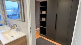 Modernes Bad mit Holzwaschtisch und Nebenraum mit dunklen Schränken und offenen Regalen.