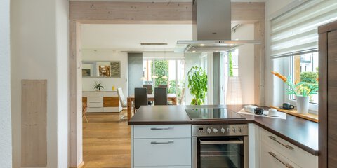 Moderne Küche mit Geräten aus Edelstahl, Arbeitsplatten aus Holz und Blick in einen hellen Essbereich.