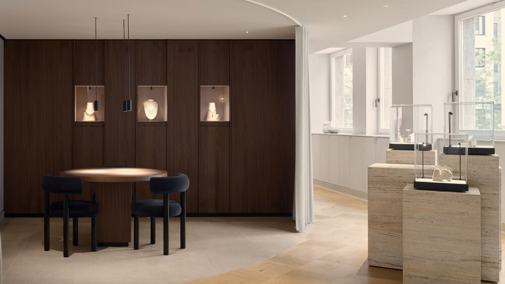 Modern showroom with jewellery display, a round table with chairs and soft daylight through large windows.