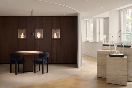 Modern showroom with jewellery display, a round table with chairs and soft daylight through large windows.