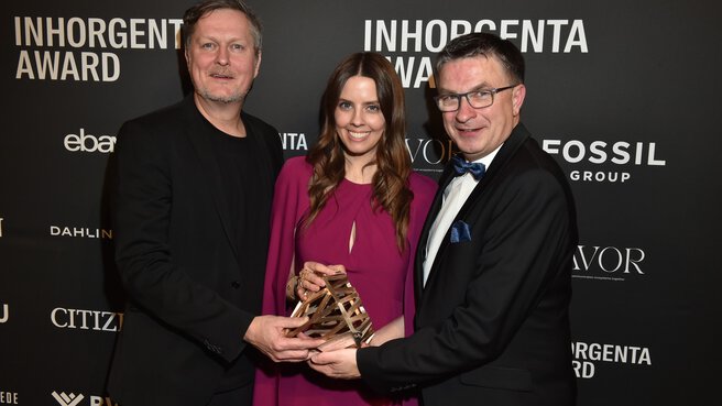 Three beaming people with the trophy for the Next Generation Retail category at the AWARD Gala in front of a logo wall.