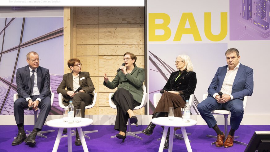 Auf der BAU sitzen drei Frauen und zwei Männer in eleganter Kleidung mit Mikrofonen auf einer Bühne und unterhalten sich.