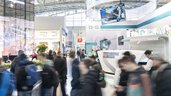 Dynamisches Bild von Menschen vor einem Messestand in der Halle.
