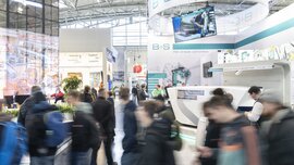 Dynamisches Bild von Menschen vor einem Messestand in der Halle.