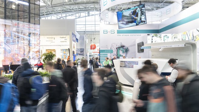 Dynamisches Bild von Menschen vor einem Messestand in der Halle.