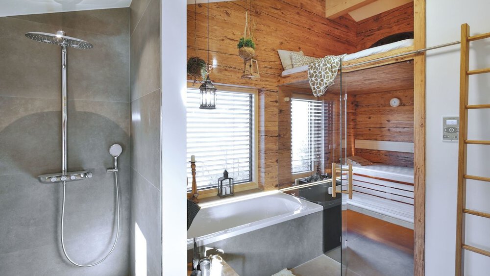 Modernes Badezimmer mit Dusche, weißem Waschbecken und Holzregalen. Helle Holzböden und -wände sorgen für eine warme Atmosphäre.