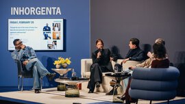 Several people holding a microphone are sitting on a stage at INHORGENTA, with three designer tables in front of them.