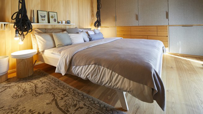 Gemütliches Schlafzimmer mit großem Bett, weichen Kissen, warmer Beleuchtung und einem flauschigen Teppich auf Holzboden.