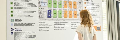 Person betrachtet einen großen Geländeplan der Messe München für mehrere Fachmessen, hält dabei einen Besucherführer in der Hand.