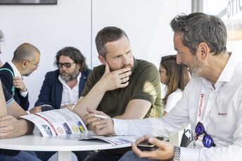 Mehrere Personen sitzen an einem Tisch und sprechen miteinander. Auf dem Tisch liegen Unterlagen.