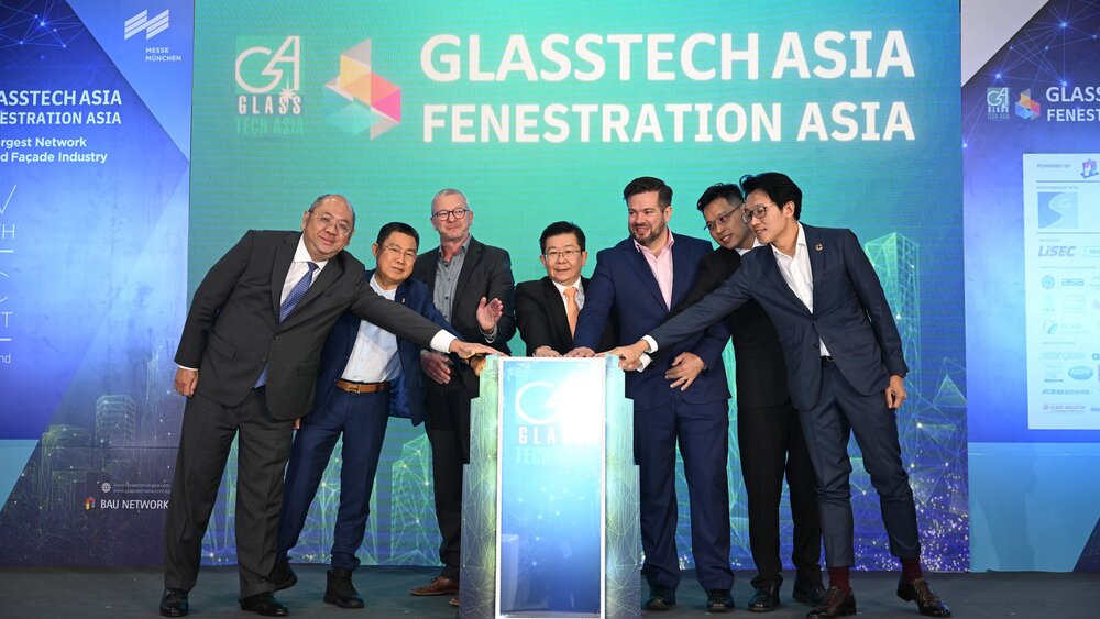 Sieben Männer in Anzügen stehen um ein Rednerpult herum und haben alle eine Hand daraufgelegt. Hinter ihnen steht „GLASSTECH ASIA FENESTRATION ASIA“.