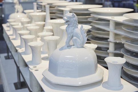 White ceramic bowls and vases arranged on shelves with a striking lion sculpture in the center.