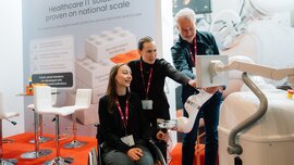 Zwei Frauen und ein Mann testen gemeinsam eine digitale Anwendung oder Robotiklösung an einem Messestand