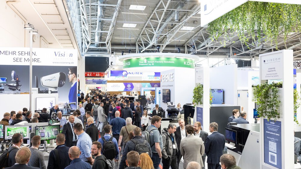 A well-attended exhibition hall with numerous stands from various suppliers featuring advertising walls and monitors.