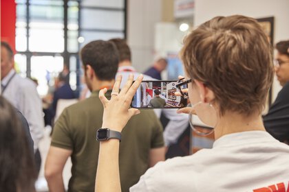 Person taking a photo with a cell phone in a busy indoor area.