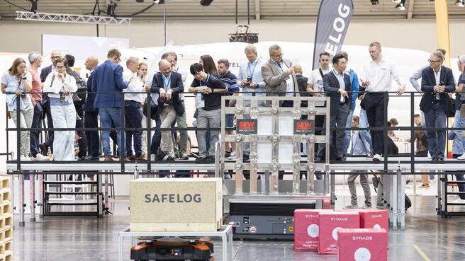 A group of people are standing on a platform in front of a demonstration area for robots in an exhibition hall.