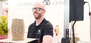 Aussteller präsentiert eine 3D-gedruckte Keramikvase an einem Messestand.