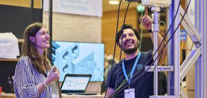 A university employee enthusiastically explains a technical test facility to a trade fair visitor.