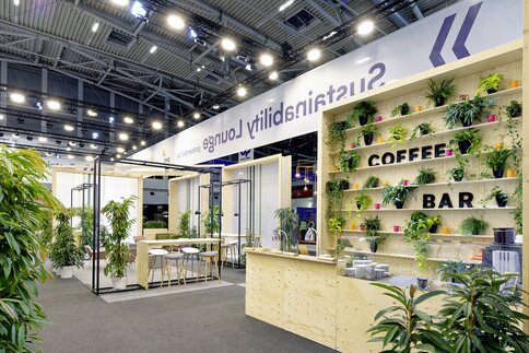 Modern coffee bar with potted plants and seating area under bright lights at an event on the topic of sustainability.