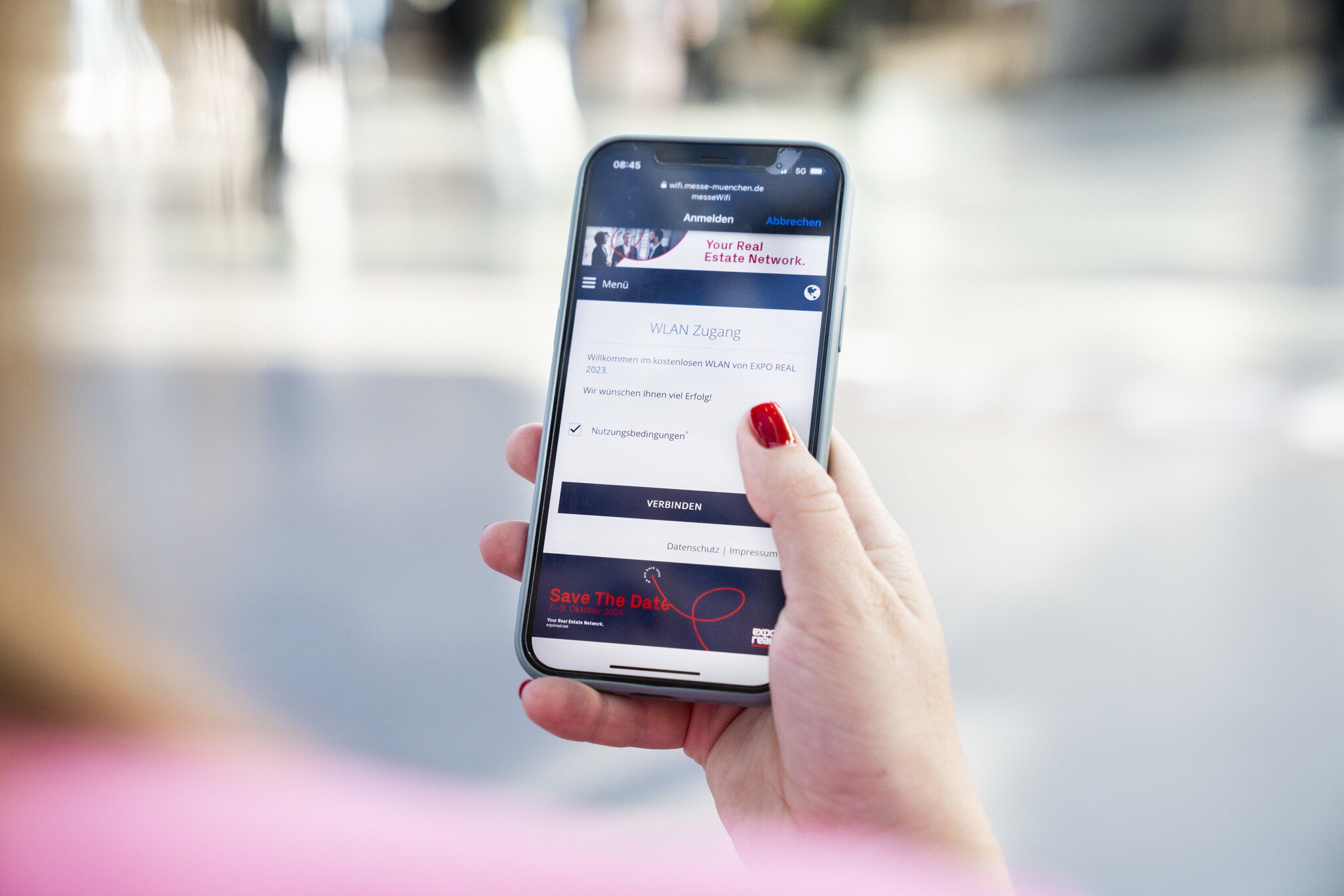 One person is holding a cell phone showing the EXPO REAL WLAN login screen.