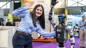 An employee poses smiling next to a humanoid robot at the trade show booth.