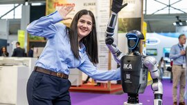 An employee poses smiling next to a humanoid robot at the trade show booth.