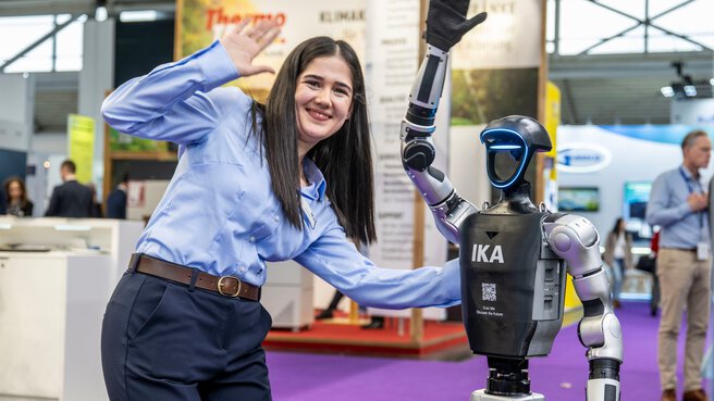 An employee poses smiling next to a humanoid robot at the trade show booth.