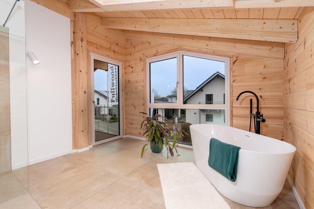 Modernes Badezimmer mit Holzwänden, freistehender weißer ovaler Badewanne, großen Fenstern und Topfpflanze.