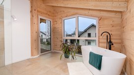 Modernes Badezimmer mit Holzwänden, freistehender weißer ovaler Badewanne, großen Fenstern und Topfpflanze.