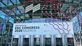 Blick auf eine Eingangshalle der Messe München zum ESC Congress 2026 mit einer passend dekorierten Glasfassade mit sechs Drehtüren darin.